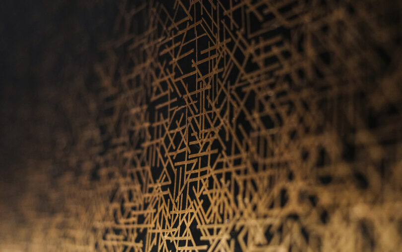 Abstract geometric pattern with intersecting gold lines on a dark background, creating a complex, web-like design.