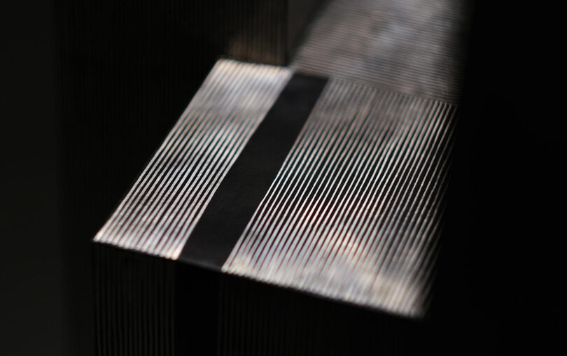 Close-up of evenly spaced vertical lines with a horizontal black band across them, creating an abstract pattern with light and shadow.