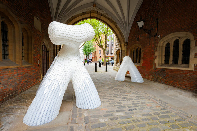 Under the vaulted archway on a cobblestone path between brick walls, two large, white abstract sculptures resembling crossed arches stand proudly, reminiscent of the innovation celebrated at the CDW 2025 Product Awards.