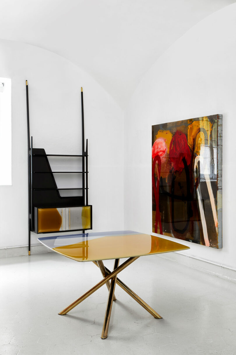 L'intérieur moderne a une table géométrique, une peinture abstraite sur le mur et une unité d'étagère noire et jaune inspirée de Draga & Aurel qui se place sur un fond blanc croustillant.