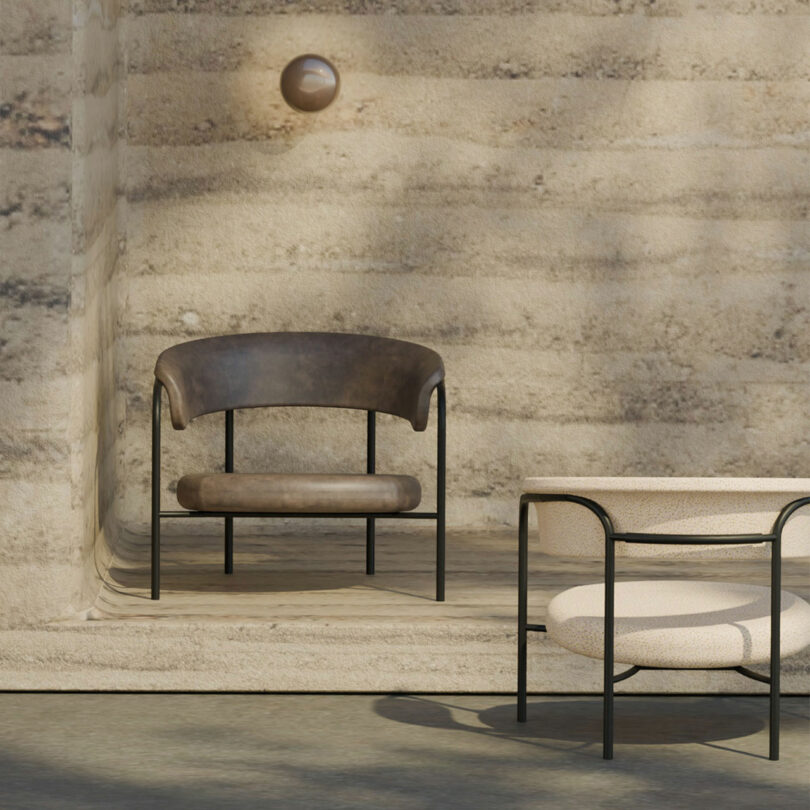 Two modern chairs, one with a dark leather seat and the other with a light fabric cushion reminiscent of Rikke Frost's style, are placed on a stone patio. A round wall light is mounted above them on the textured wall.