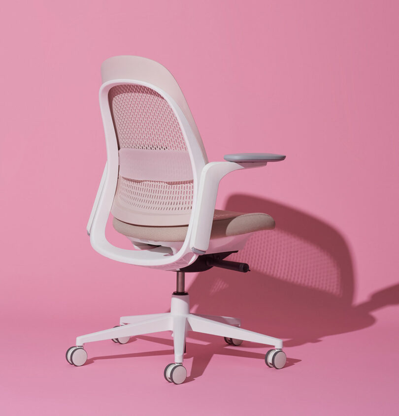 Modern office chair with a mesh backrest and cushioned seat on a pink background, featuring adjustable armrests and a wheeled base.