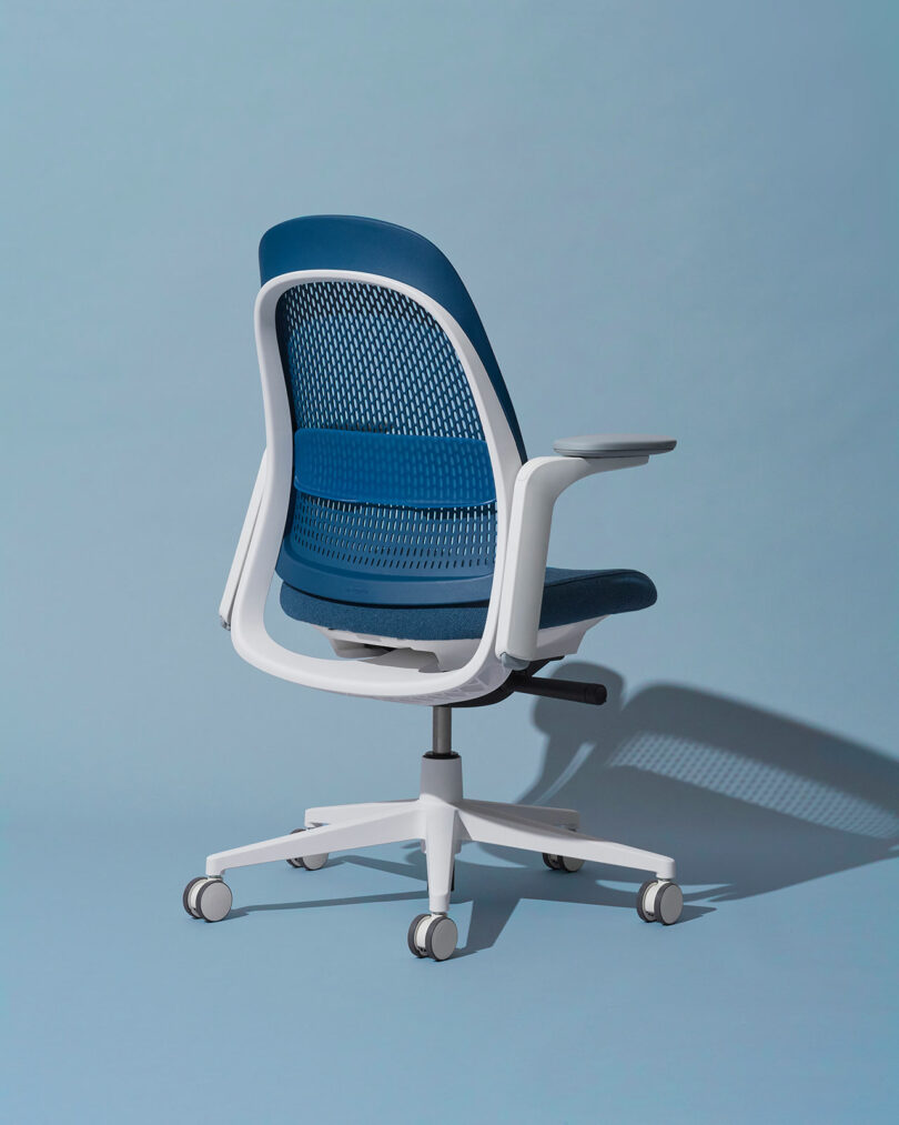 A blue and white office chair with wheels is positioned against a light blue background. The chair is shown from the back and slightly to the side, highlighting its design and structure.