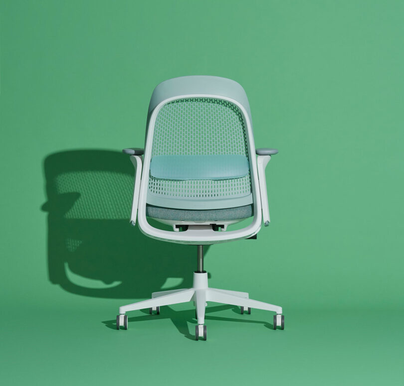 Light blue and white office chair on wheels against a green background, casting a shadow to the left.