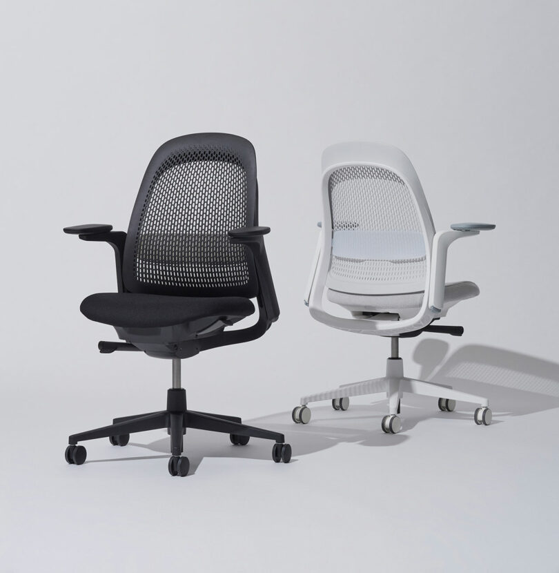 Two ergonomic office chairs with mesh backs, one black and one white, on a plain background. They have armrests and wheeled bases.