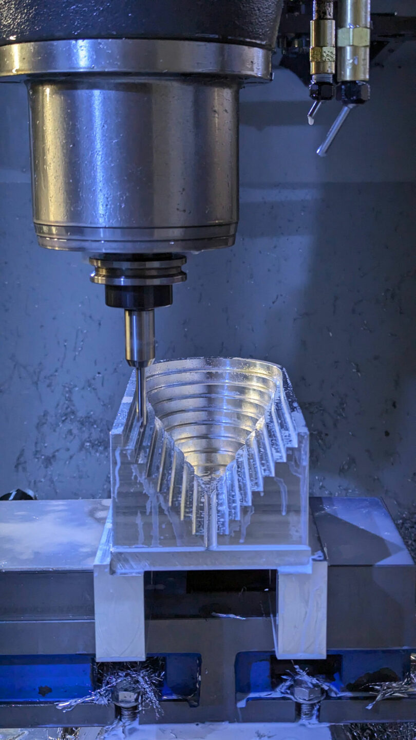 A CNC machine is milling an intricate, stepped pattern into a block of metal.