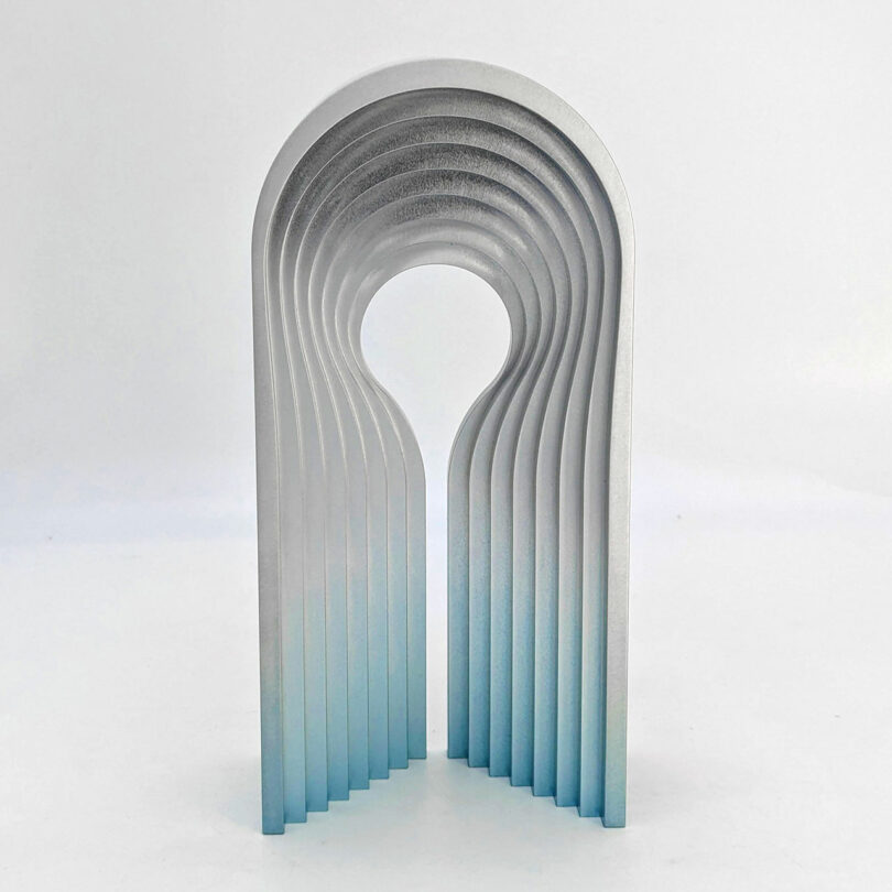 A modern, abstract sculpture with overlapping arches creating a tunnel effect, featuring a gradient from silver to blue at the base.