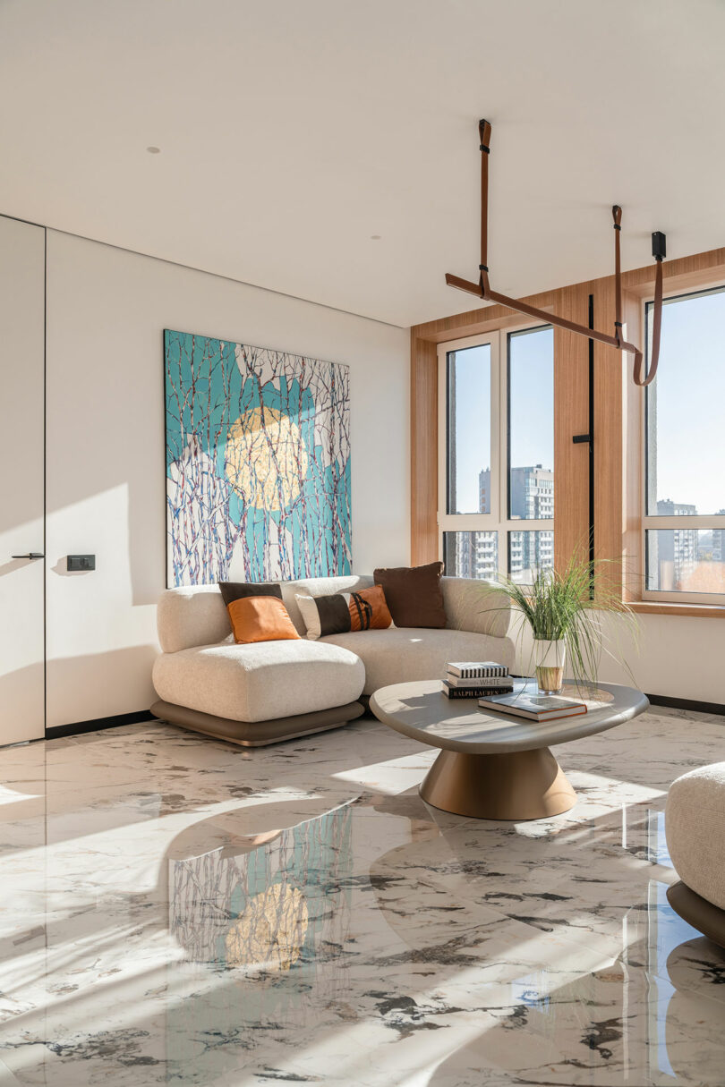 Modern living room with a marble floor, white sofa, round coffee table, and large windows. A colorful abstract painting is on the wall, and city skyline is visible outside.