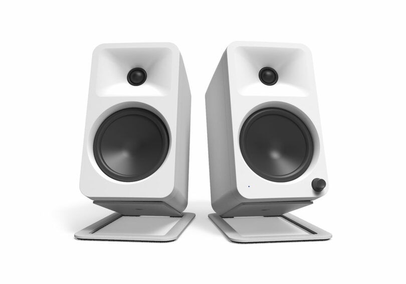 Two white Kanto Audio speakers on stands with a modern design showcase large woofers and smaller tweeters, set against a plain white background.