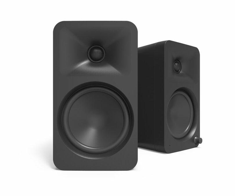 Two sleek black speakers from Kanto Audio, one angled slightly behind the other, stand against a white background. Each features a large circular woofer and a smaller tweeter above, delivering crisp sound and modern design.