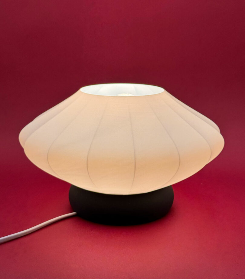 A round, white fabric lamp with a dark base against a red background.