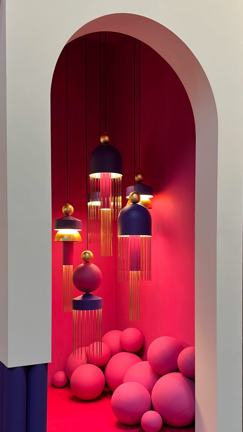 A vibrant pink and red room, reminiscent of a Maison&Objet showcase, features hanging modern pendant lights and various sized spherical decorations, creating a bold and artistic atmosphere.