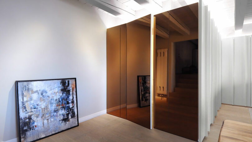 Modern hallway with brown reflective panel doors, framed abstract paintings, and light wood flooring.