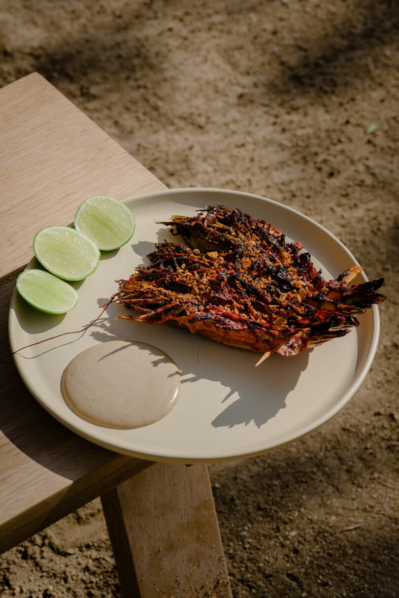 Grilled dish served with lime wedges and a creamy sauce on a round beige plate.