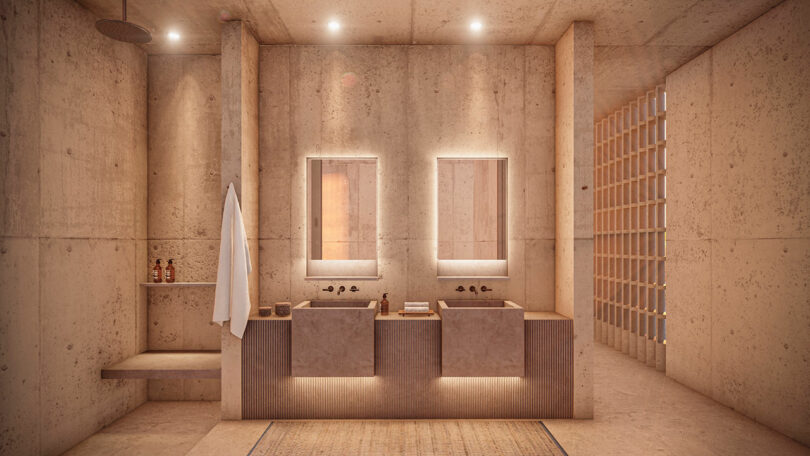 Modern bathroom with concrete walls and floor, dual sinks, and illuminated mirrors. A towel hangs on the wall. Three decorative bottles sit beside the sinks. Subtle lighting illuminates the space.