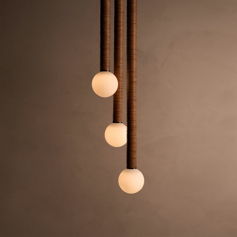 Three spherical pendant lights with a warm glow, inspired by Studio Luddite's signature style, hang vertically against a neutral background.