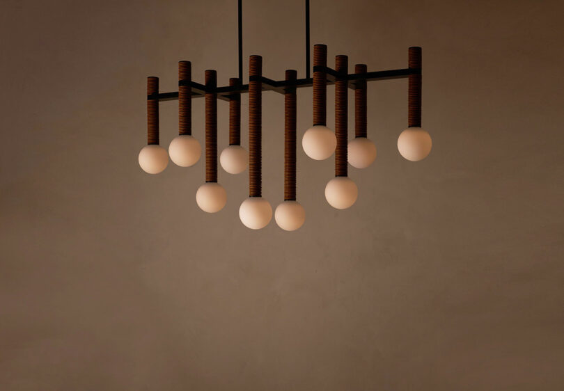 A Pell Chandelier by Studio Luddite features twelve spherical bulbs elegantly suspended against a plain beige wall.