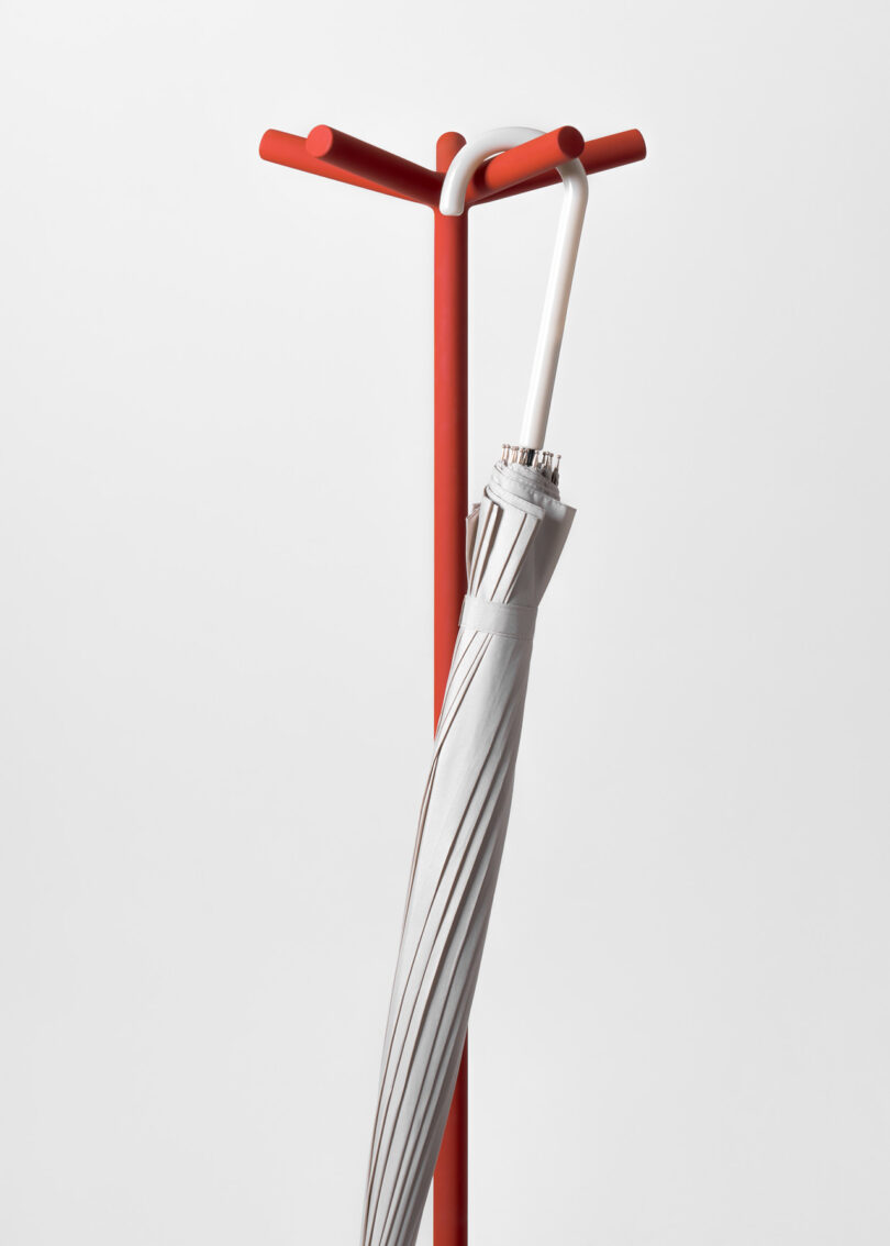 A closed gray umbrella hangs on a red stand against a plain white background.