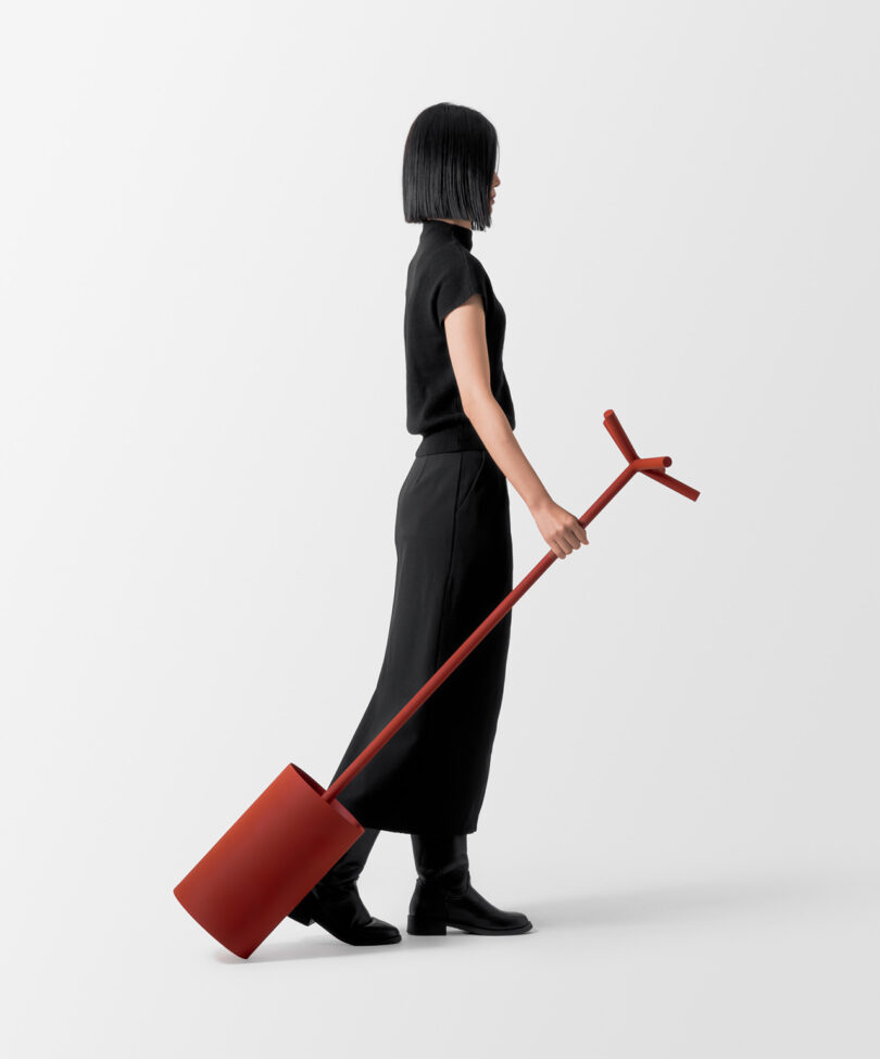 A person in black attire pulls a large, red, umbrella stand on a white background.