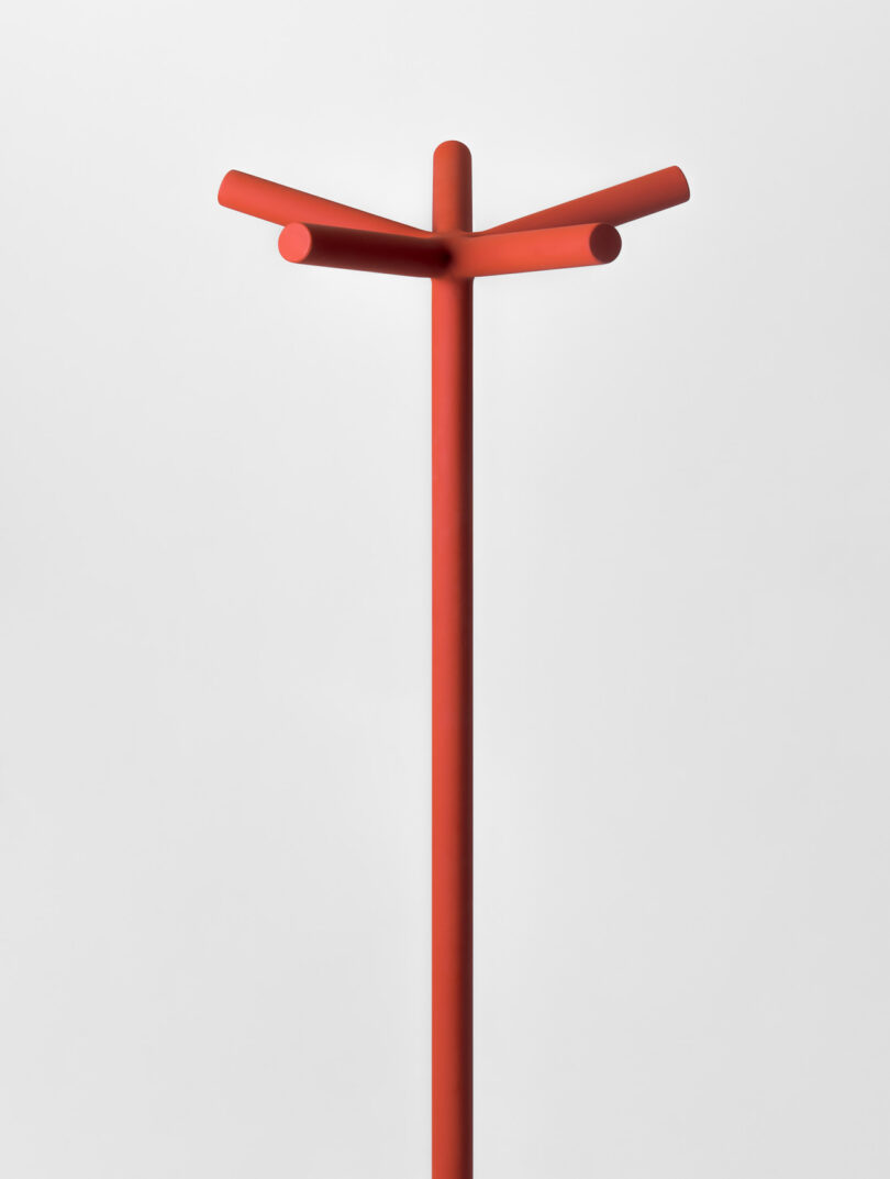 A minimalist red coat rack with three horizontal prongs on a white background.