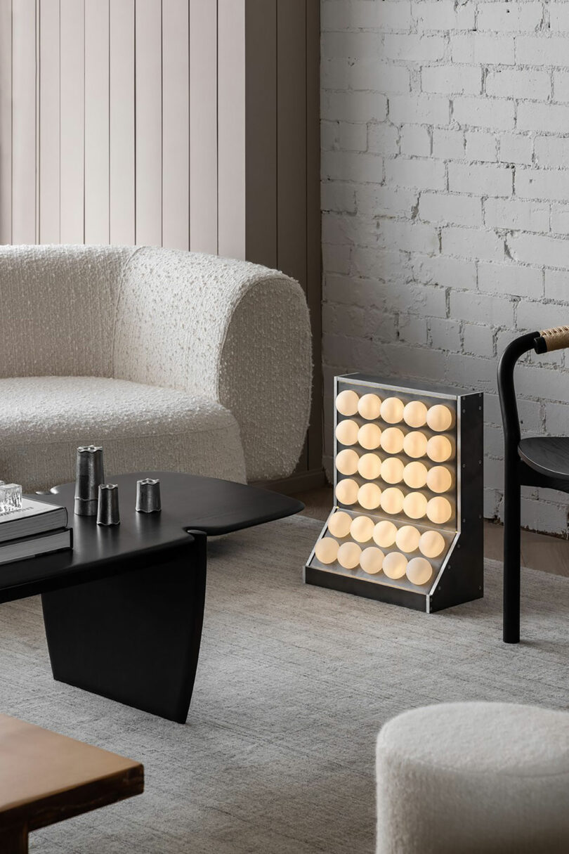 Modern living room with a white sofa, black table, and a unique Rider Objects for Thought lamp featuring circular lights against a white brick wall.