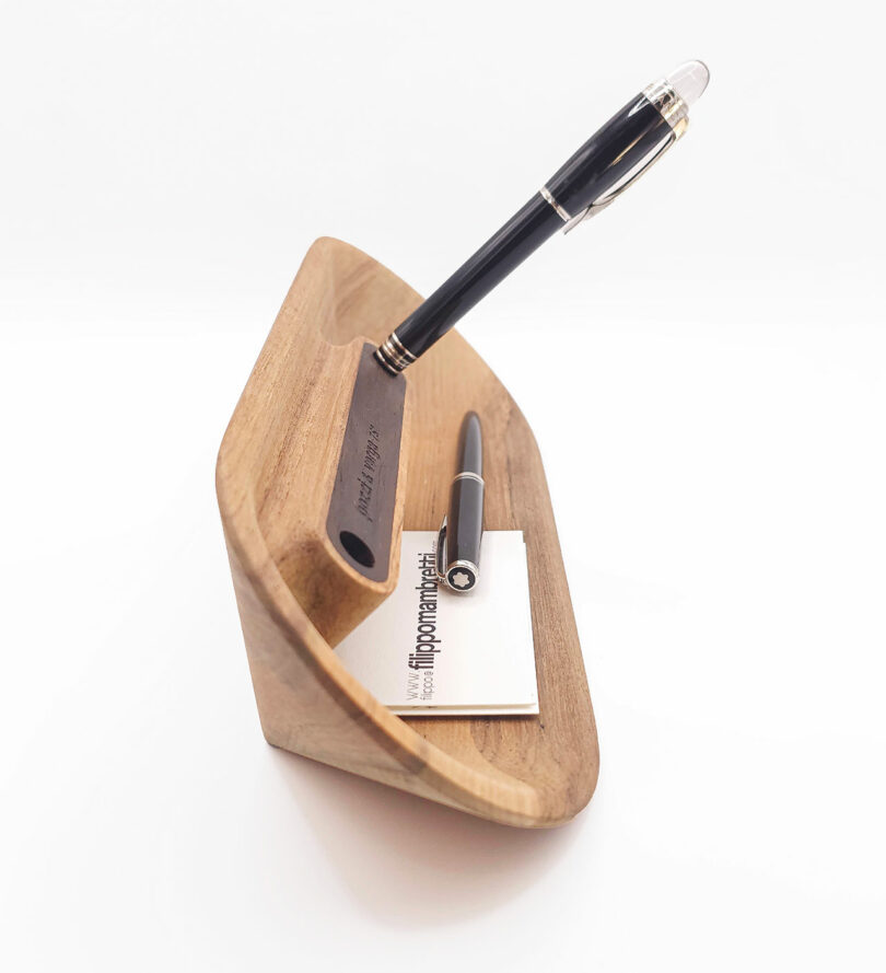 Wooden pen holder with a vertical slot for one pen and a horizontal groove for another pen, holding a small stack of business cards.