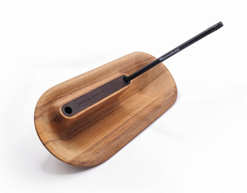 A wooden incense holder with a minimalist design, featuring a black incense stick inserted at an angle.