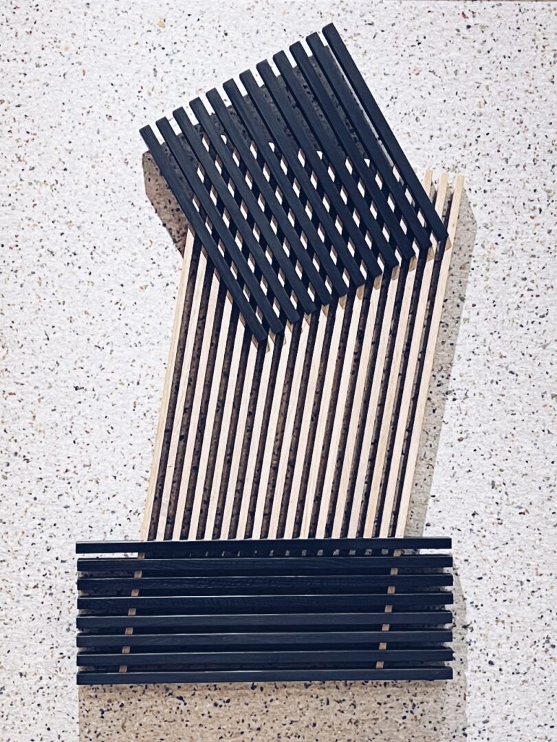 A geometric pattern reminiscent of "Take Five" emerges with alternating black and beige wooden slats arranged diagonally on a speckled surface.