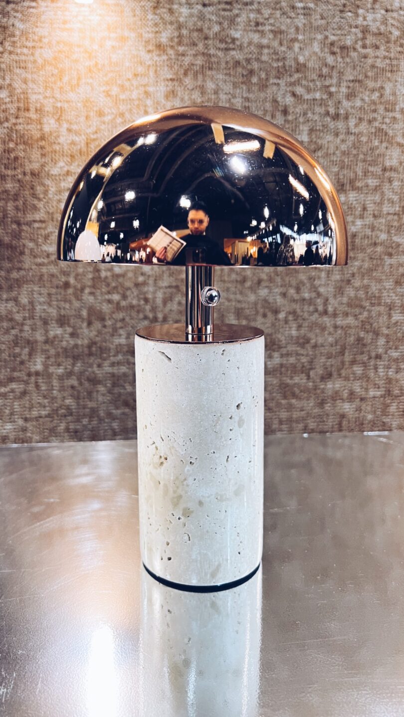 A modern table lamp with a cylindrical stone base and a reflective half-dome metal shade, capturing the serene ambiance of a "Take Five" moment in its blurred indoor reflection.