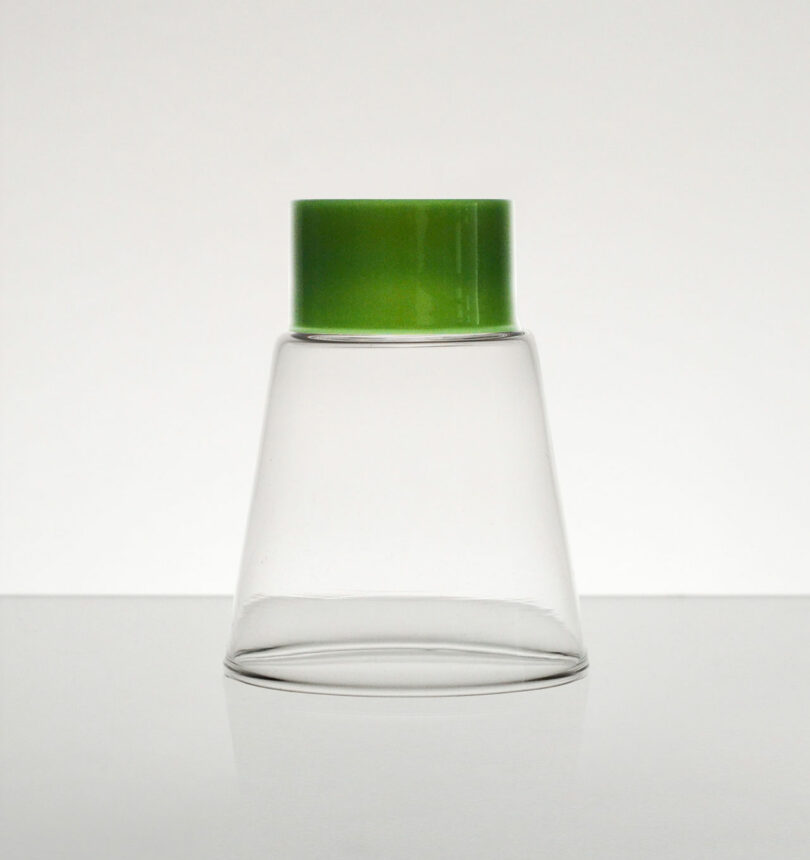 A clear Podio glass container with a wide base tapers to a green screw cap at the top, set against a plain white background.