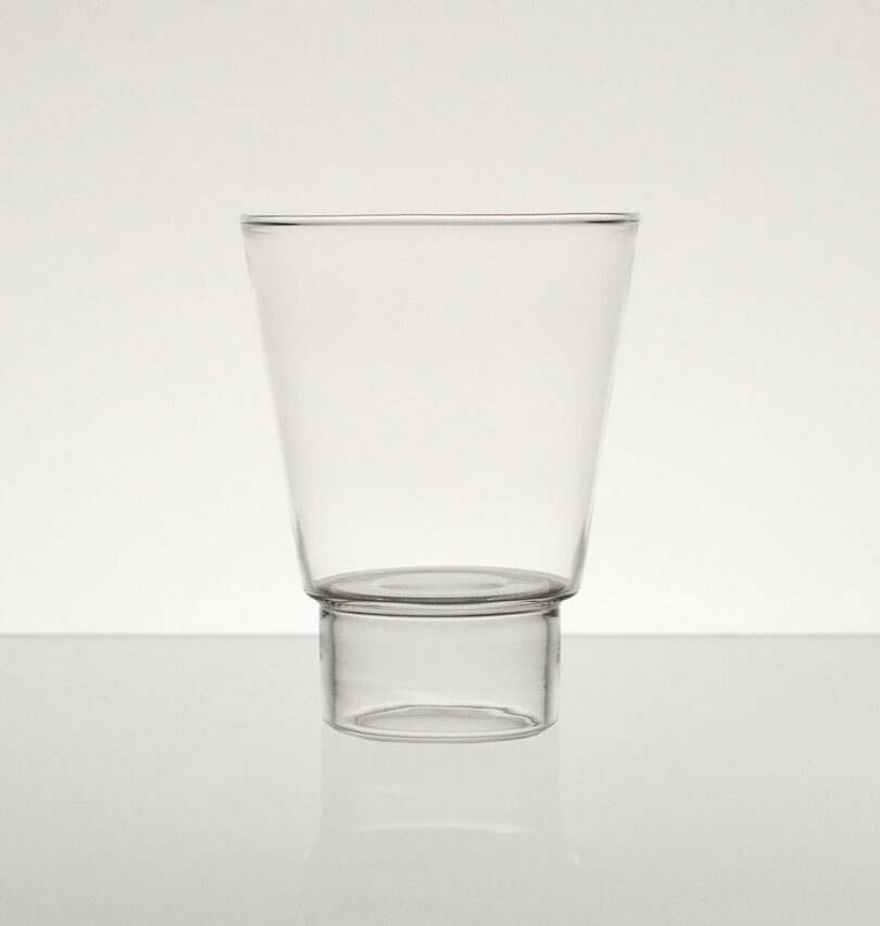 The Podio glass, with its modern tapered design, sits elegantly on a plain surface against a neutral backdrop.