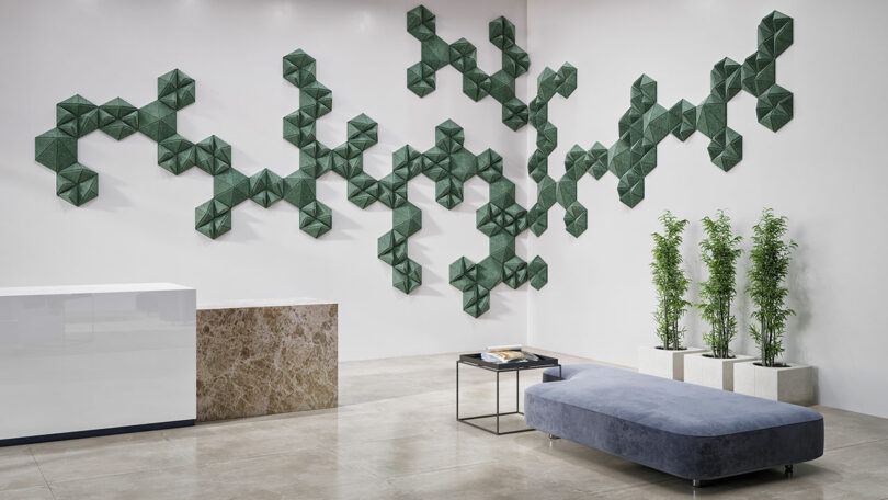 The modern interior features Unika Vaev geometric green wall art complemented by a marble counter, a sleek gray bench, and three potted plants on the pristine white floor.