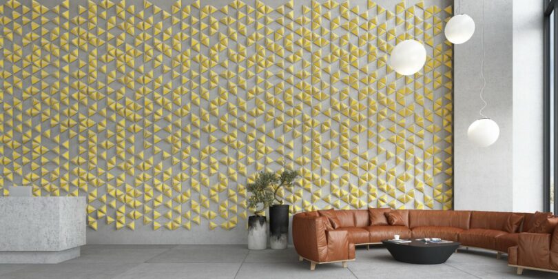 Modern lobby with geometric yellow wall art, brown leather sectional, round black table, and spherical lights. Large window on the right and plants placed near the seating area.