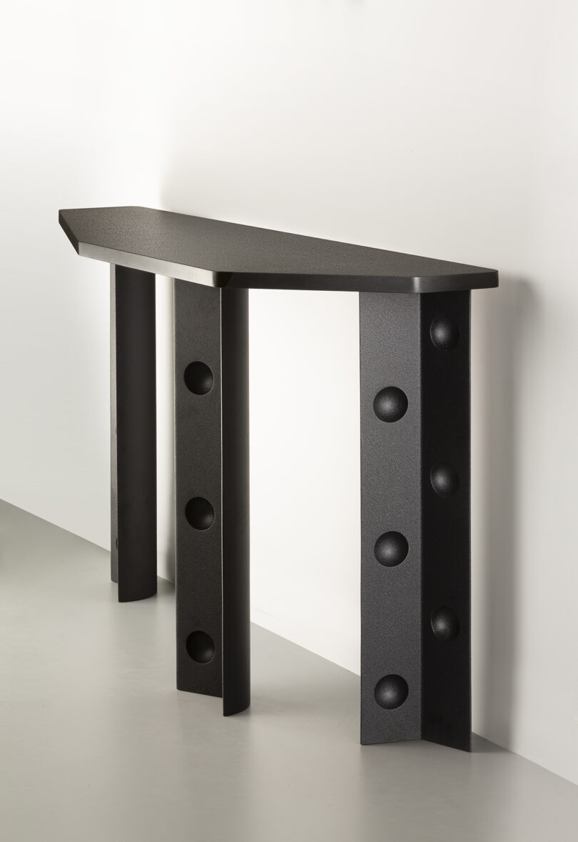 A modern black console table with a triangular top and two legs featuring circular cutouts, against a white wall.