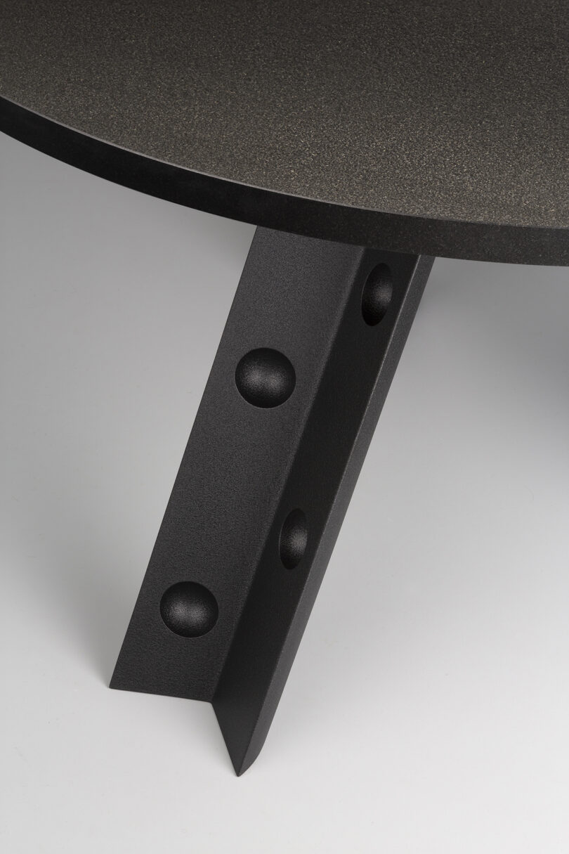 Close-up of a table with a dark, textured surface and a unique leg design featuring circular cutouts.