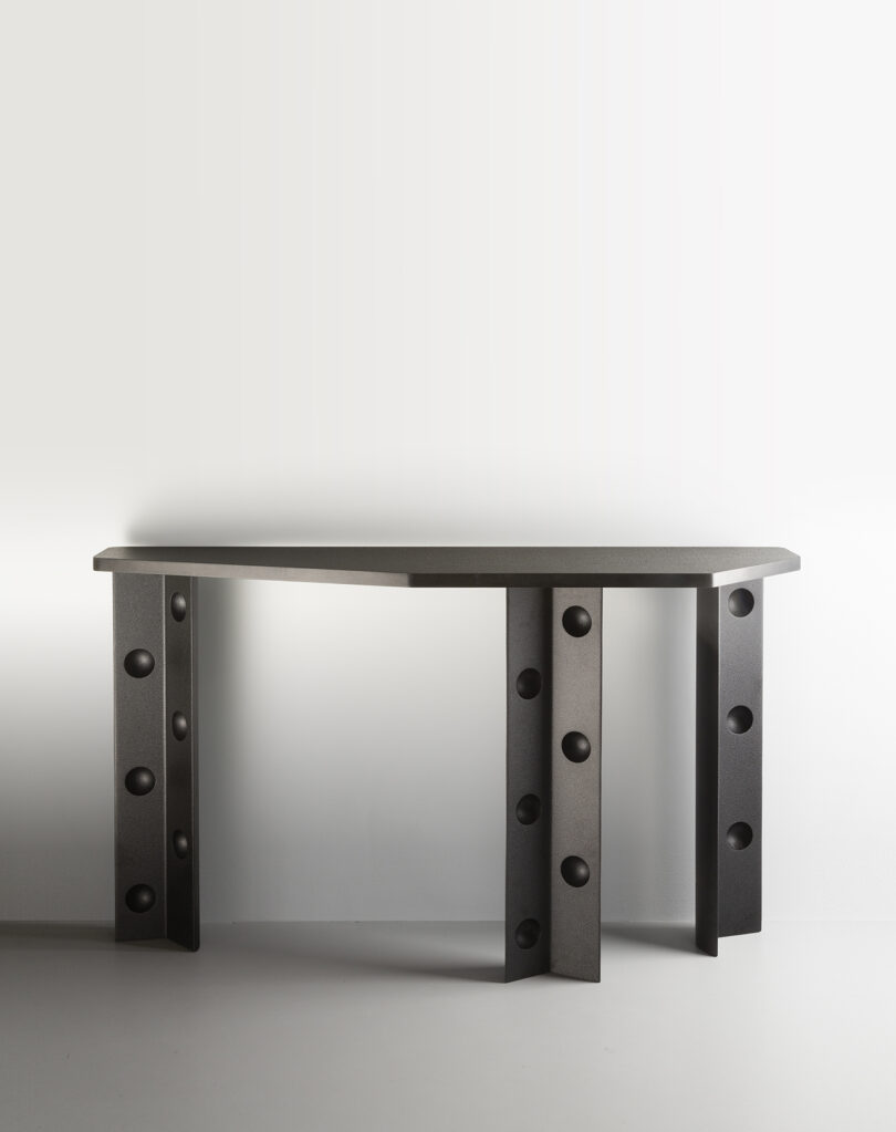 A modern black console table with a semicircular top and three legs, each featuring round cutouts.