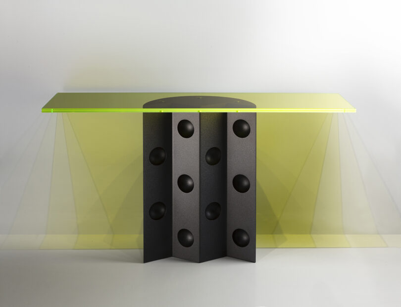 A modern console table with a translucent yellow glass top, designed by Victoria Wilmotte, features a black geometric base with circular cutouts that add a touch of elegance.