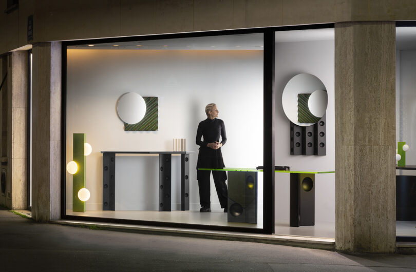 A person stands in a modern store display with mirrors, green accents, and circular light fixtures.