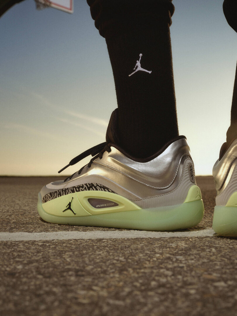 Personne debout sur un terrain de basket portant des baskets argentées et vert fluo avec des chaussettes noires arborant un logo.