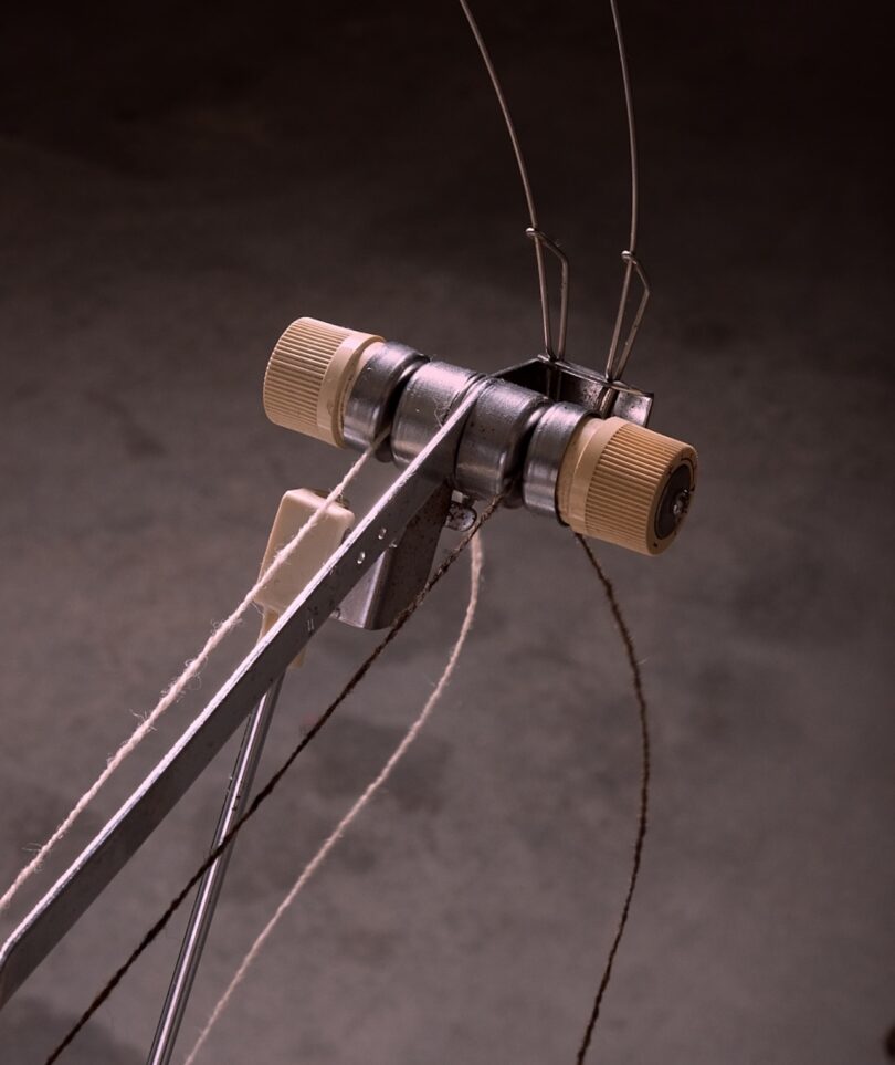 A metal yarn winder with cream-colored knobs holds two strands of yarn, against a dark background