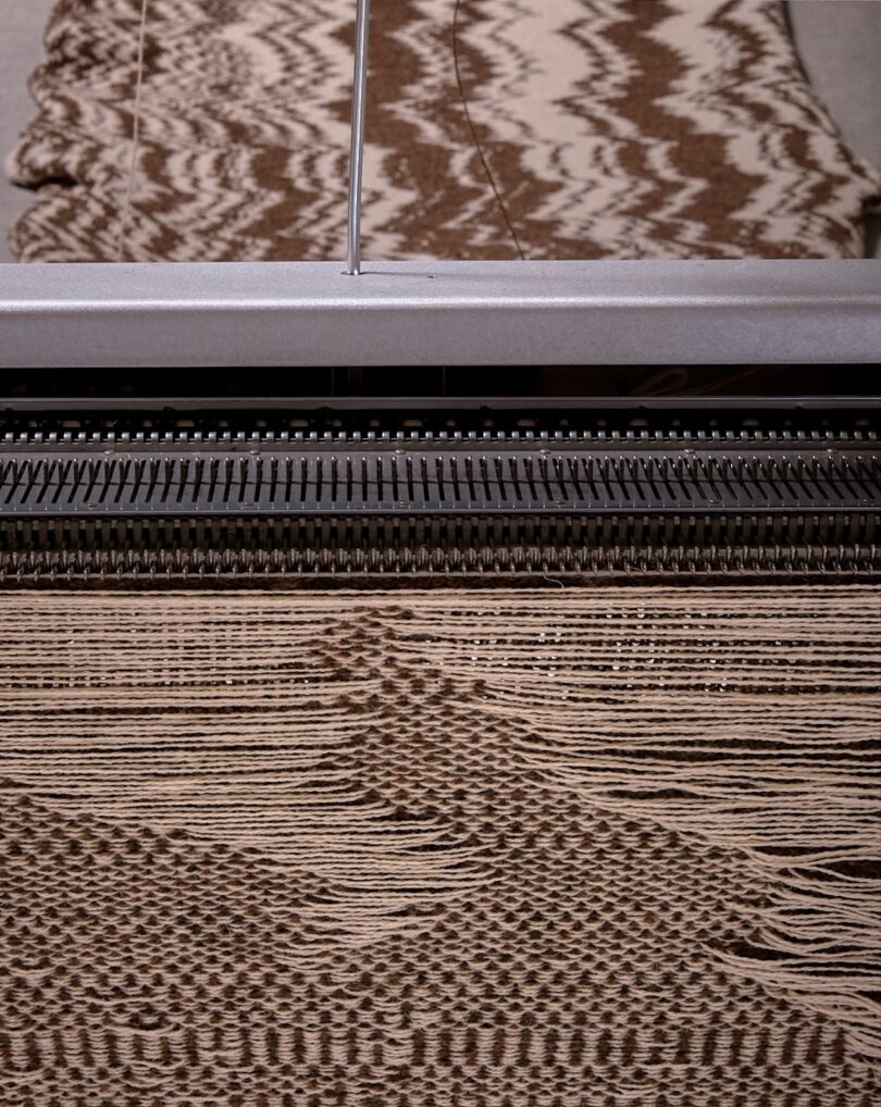 Close-up of a knitting machine producing a brown and white patterned fabric