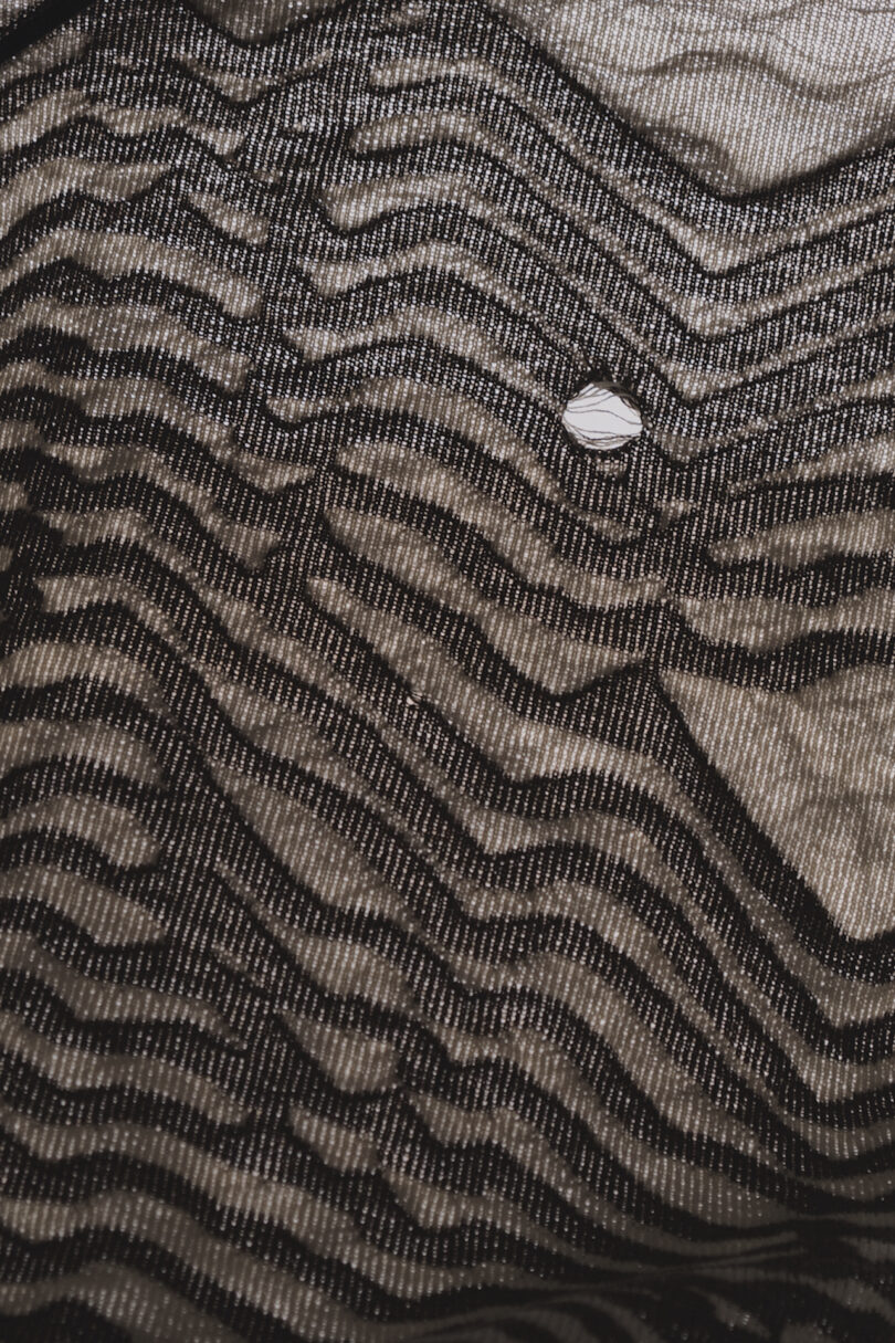 Close-up of patterned fabric with wavy, dark lines and a single small hole near the center