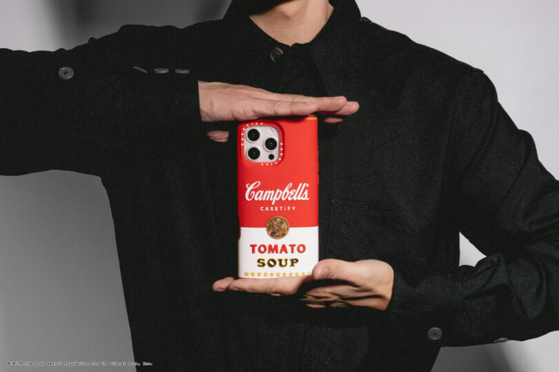 Person holding a smartphone with a red and white case resembling a Campbell's Tomato Soup can.