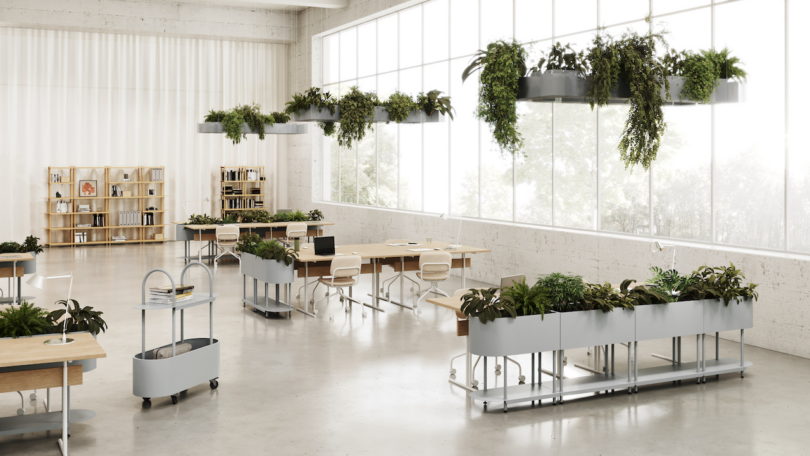 A modern office space with large windows, desks, chairs, and various plants integrated into the furniture and hanging from the ceiling