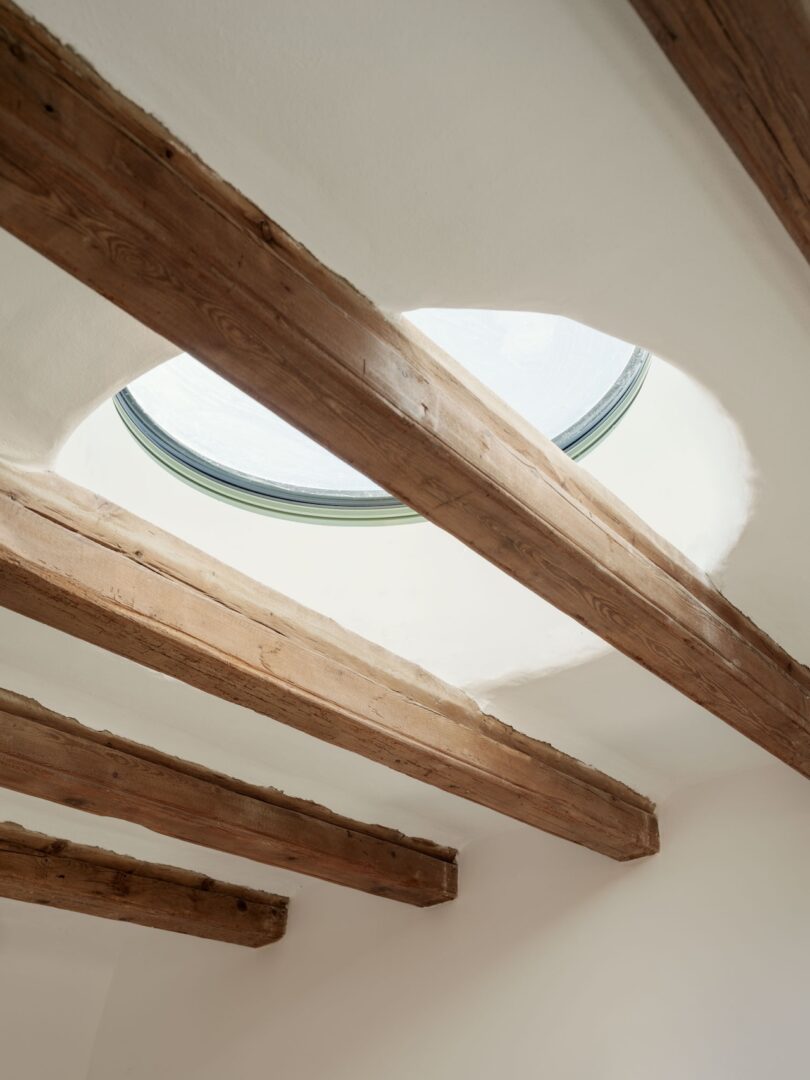 Wooden beams on a white ceiling with a circular skylight above.