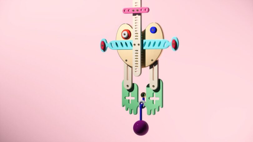 Abstract mechanical sculpture with colorful geometric shapes and components against a pink background