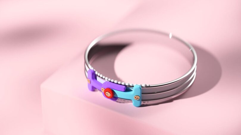 A colorful, abstract bracelet with circular and rectangular components is on a pink background.