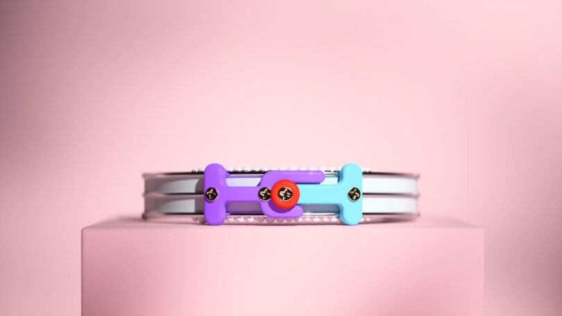 A colorful, abstract bracelet with circular and rectangular components is centered on a pink background.