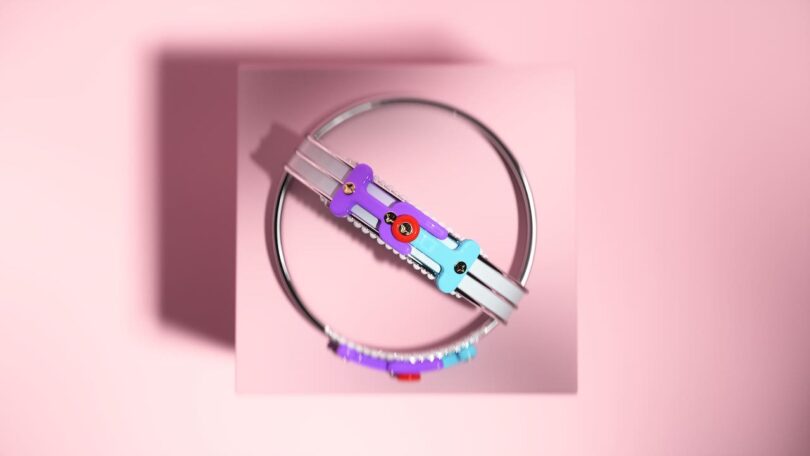 A colorful, abstract bracelet with circular and rectangular components is centered on a pink background.