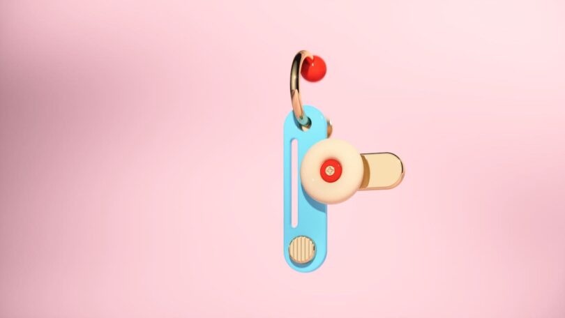 A colorful abstract earring with geometric shapes, including a blue rectangle, beige circle, and gold accents, against a pink background.